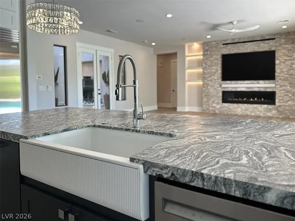 Modern kitchen with granite island, farmhouse sink, chrome faucet, and wall-mounted TV/fireplace.