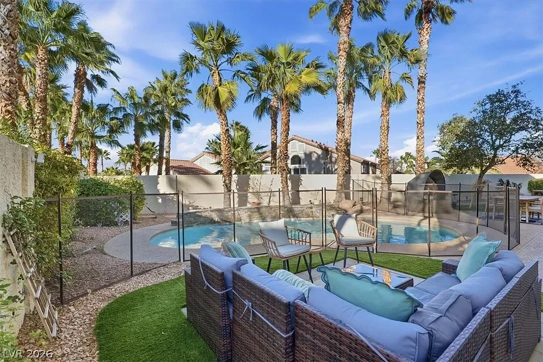 Backyard pool with palm trees, lounge chairs, and blue-cushioned patio seating at sunset