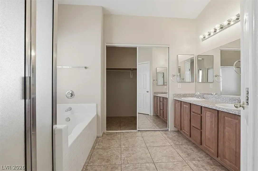 Bright bathroom with double vanity, mirrors, tub, and open doorway to a closet.
