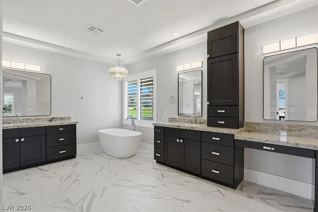 Spacious white bathroom with dark vanities, freestanding tub, large mirrors, and marble tile floor