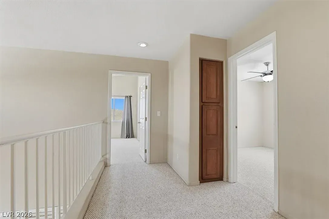 Bright upstairs hallway with white railings, beige walls, and an open doorway to a closet or bathroom.