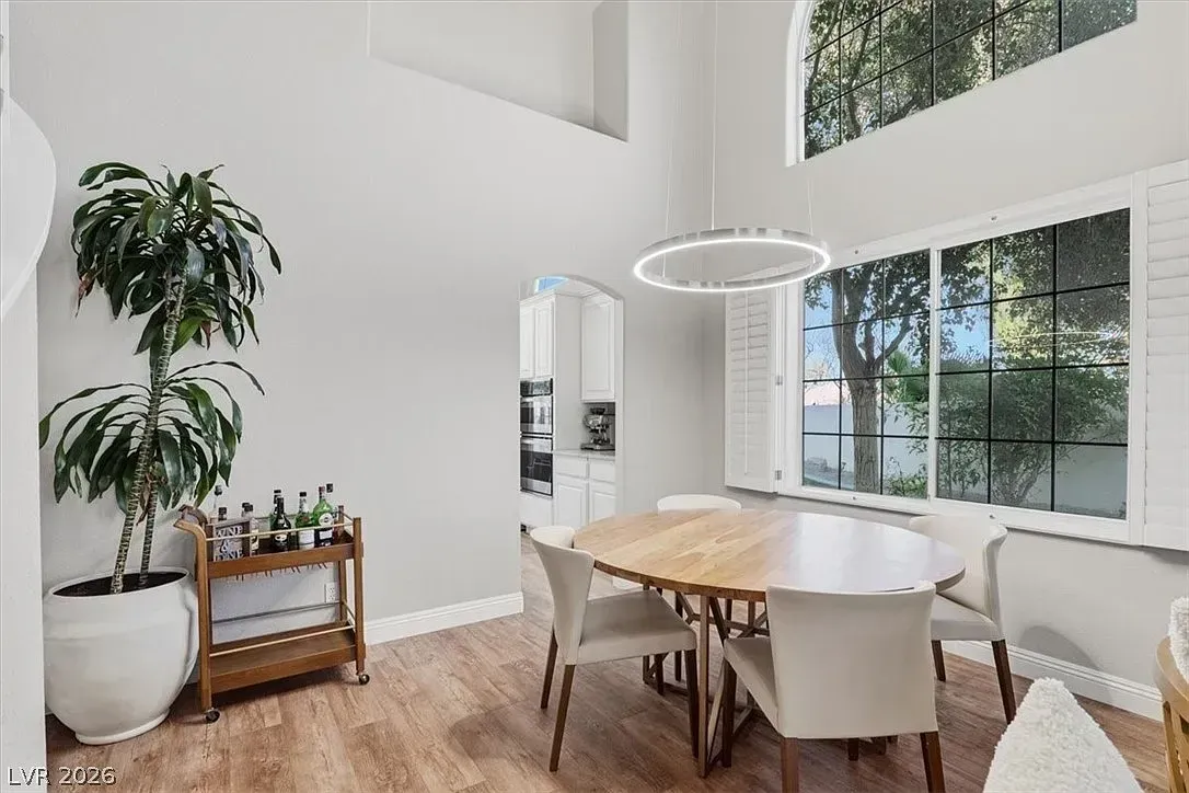 Bright dining room with a wooden table, white chairs, large windows, and a tall potted plant