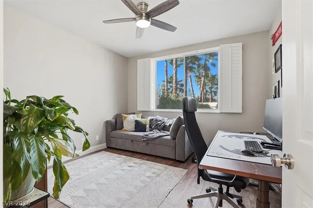 Bright home office with a desk, chair, sofa, plant, and large window by a ceiling fan.