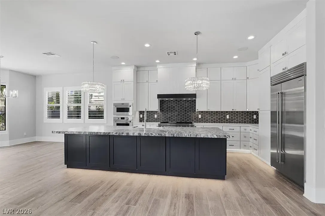 Modern kitchen with dark island, white cabinets, marble backsplash, and stainless steel appliances