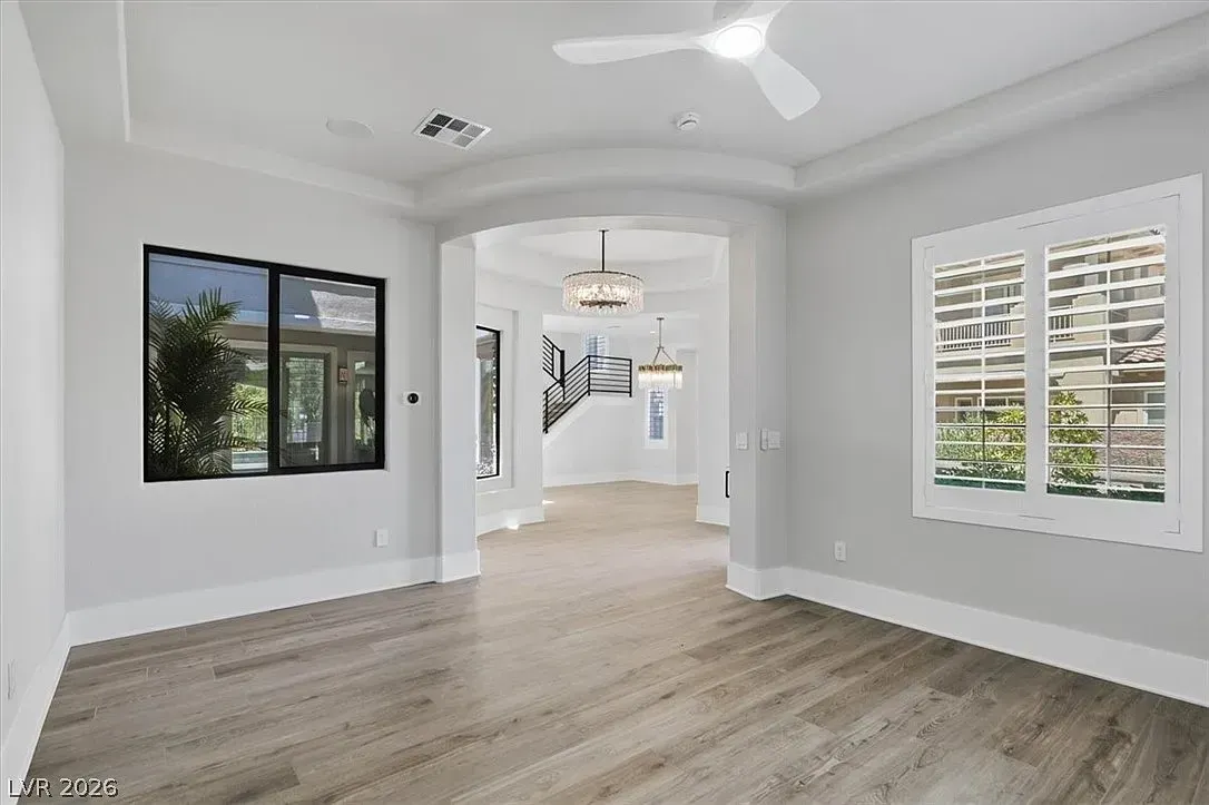 Bright empty living room with white walls, wood floors, ceiling fan, and large windows.