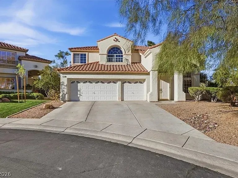 Suburban stucco house with a three-car garage, tiled roof, and desert landscaping under a blue sky