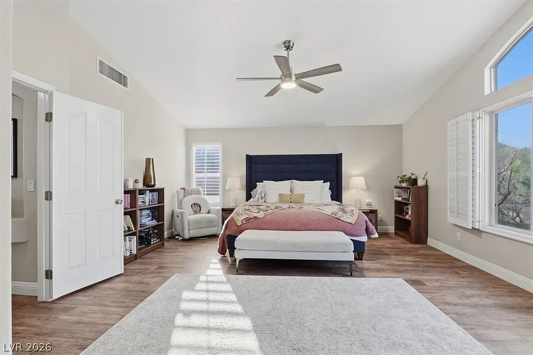Bright bedroom with a bed, ceiling fan, white walls, large windows, and a light gray rug.