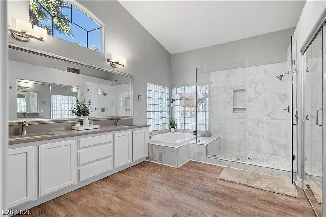 Bright bathroom with white vanity, large mirror, tiled shower, and skylight over wood-look floor.