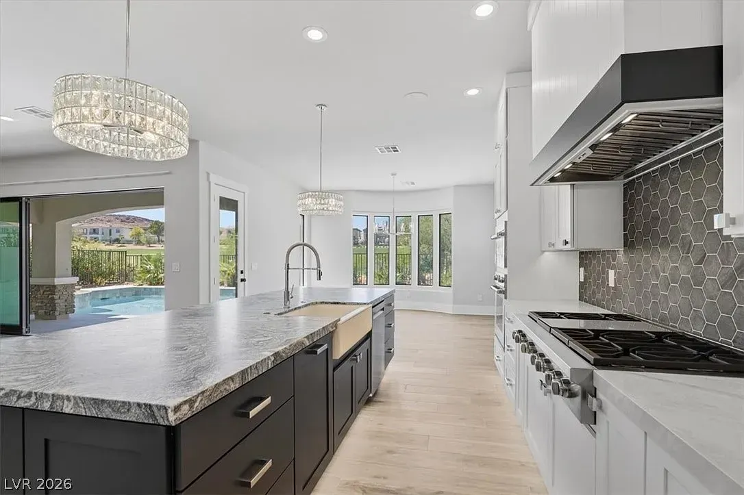 Bright modern kitchen with dark island, white cabinets, mosaic backsplash, and pool view through glass doors