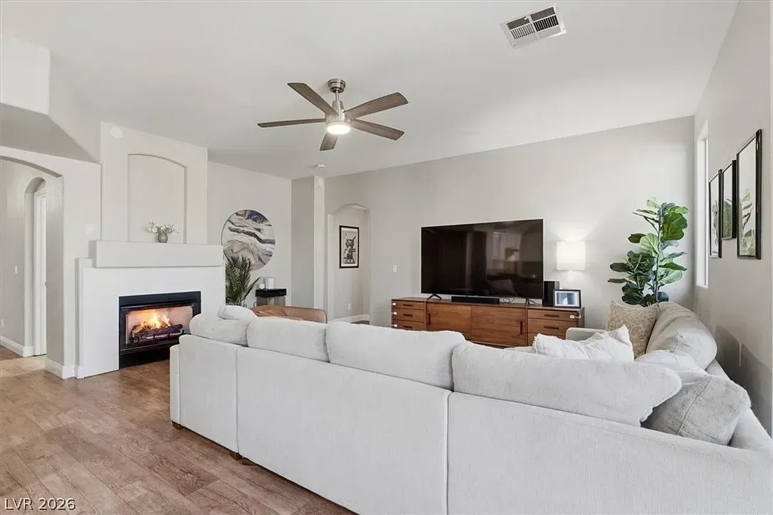 Bright living room with white sectional, fireplace, ceiling fan, and dark wood TV console.