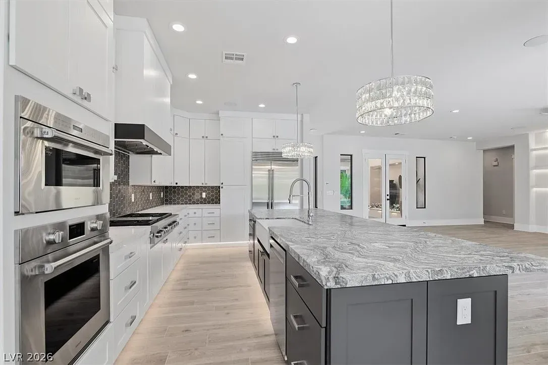 Bright modern white kitchen with marble island, built-in ovens, and open living area beyond