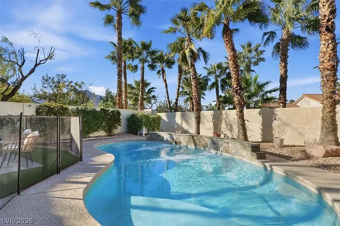 Backyard swimming pool with palm trees, stone wall, and screened enclosure under a bright blue sky