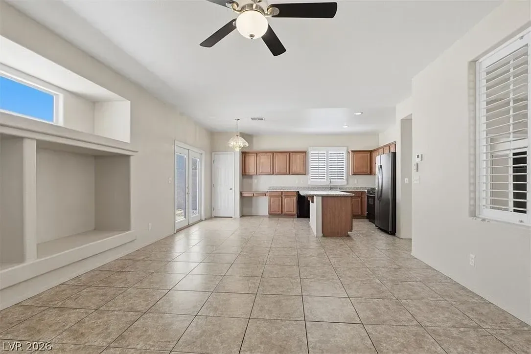 Bright open kitchen and living area with tiled floors, white walls, ceiling fan, and wooden cabinets