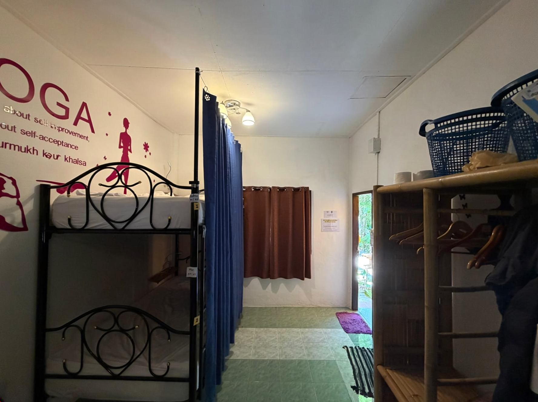 Dorm room with bunk beds, blue curtain divider, window, and shelves in a narrow interior.
