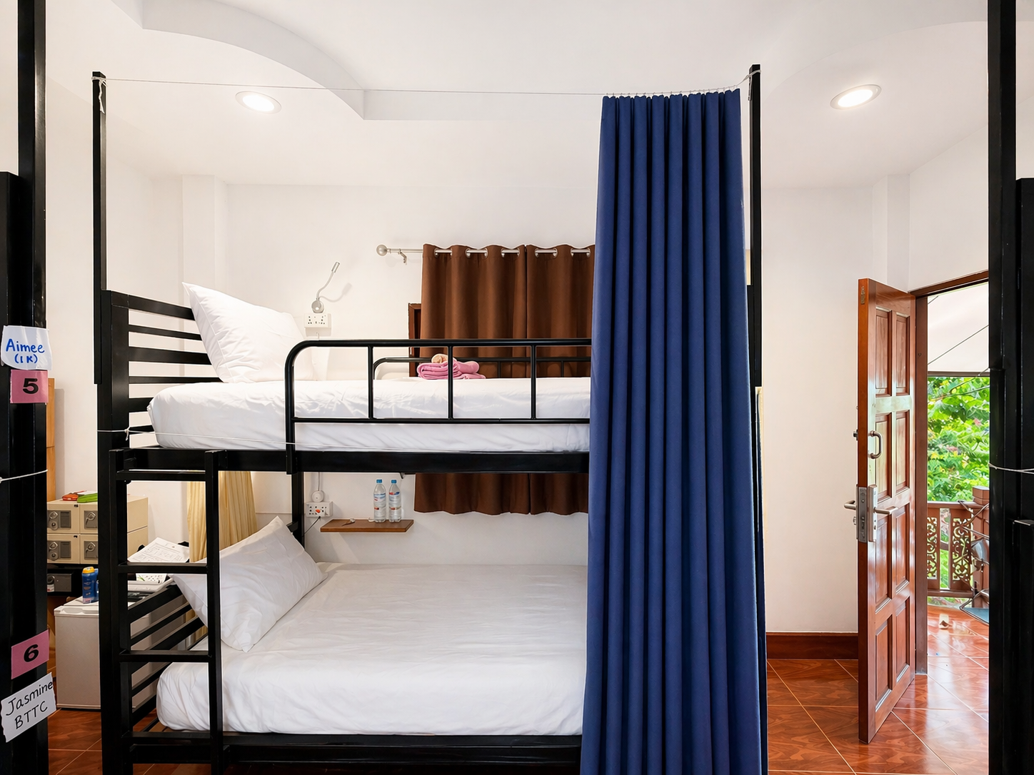 Bunk bed in a bright room with white walls, blue curtain, and open door to a balcony.