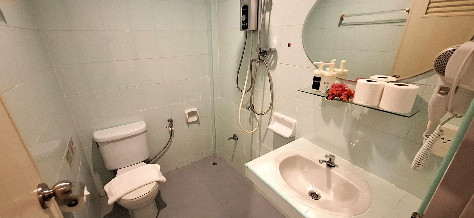 Small bathroom with toilet, sink, shower, and wall-mounted shelves for toiletries.