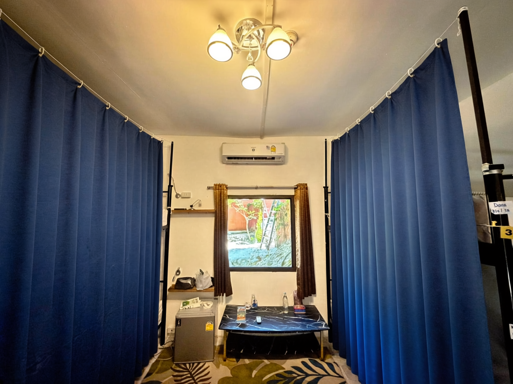 Narrow room with blue curtains, central table, wall mirror, and window at the far end.