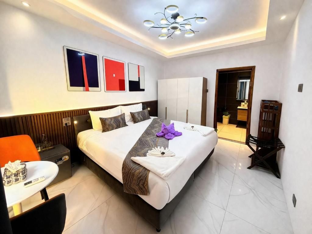Modern bedroom with a large bed, white tile floor, bedside tables, wall art, and a doorway to an adjoining room