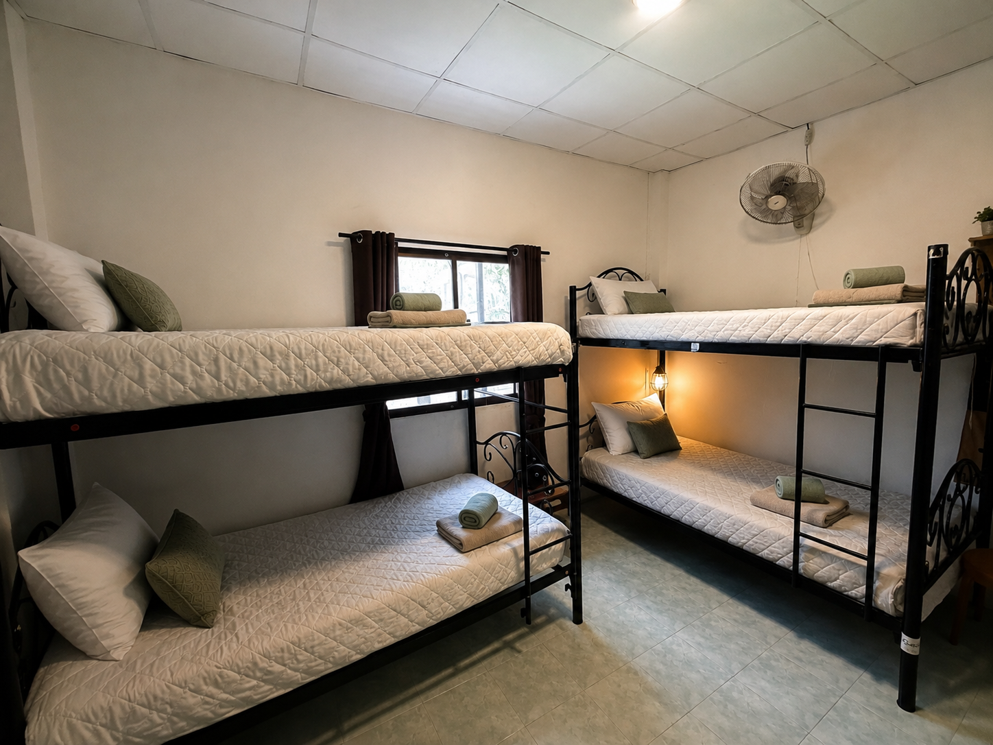 Small bedroom with two black metal bunk beds, light bedding, and a small window.