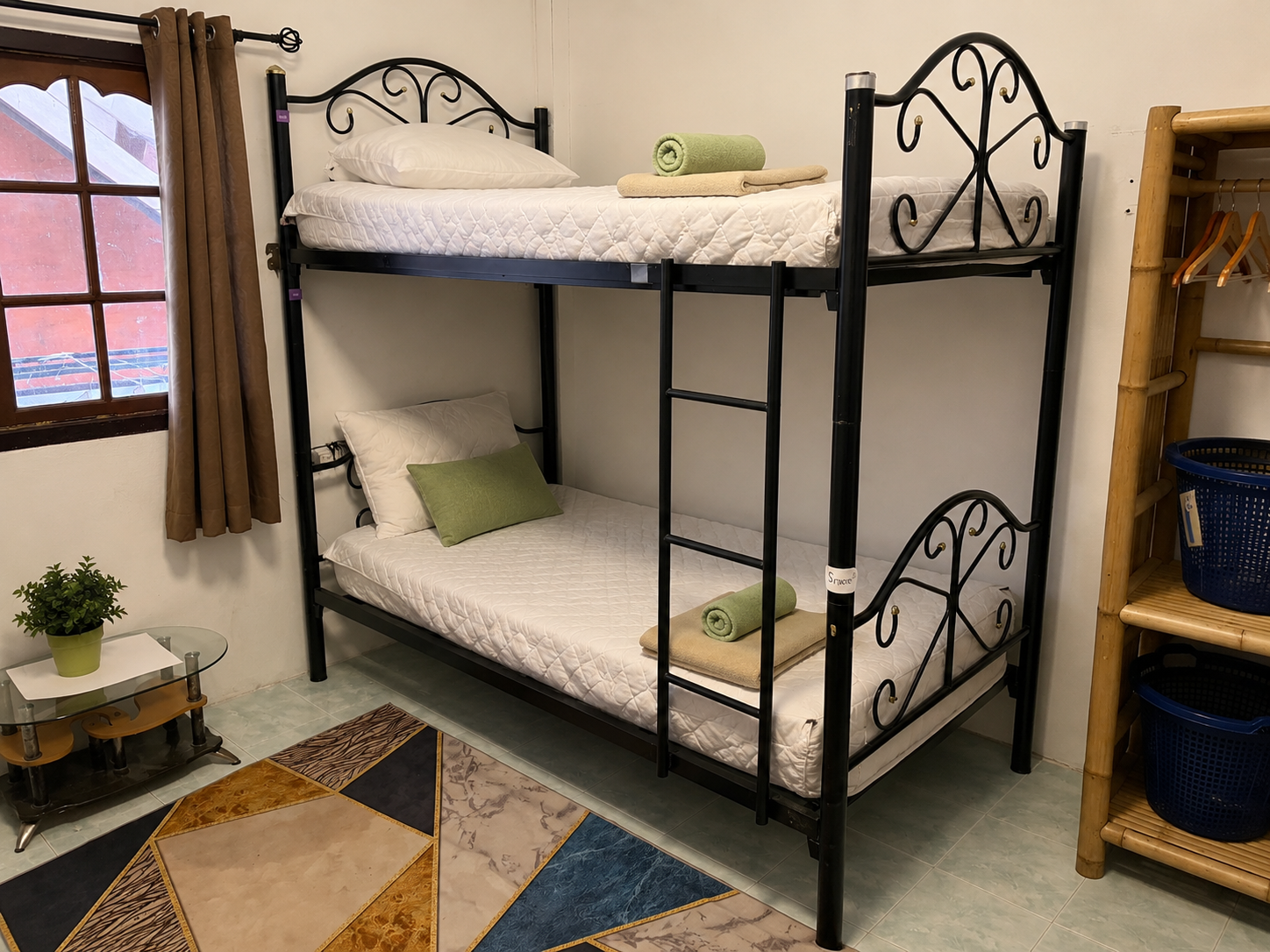 Bunk bed with black metal frame, white bedding, and green pillows in a cozy room with rug and shelf