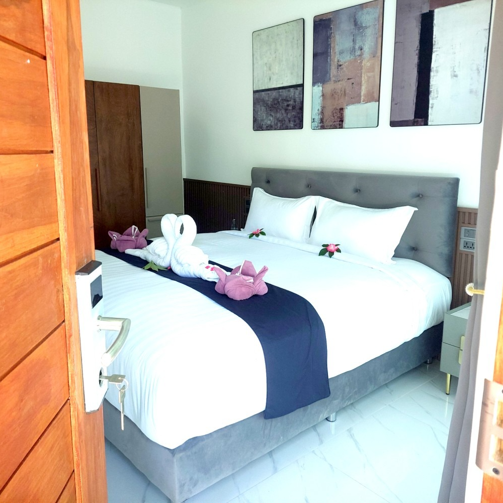 Bright bedroom with a gray bed, white bedding, navy runner, and towel swans on the bed