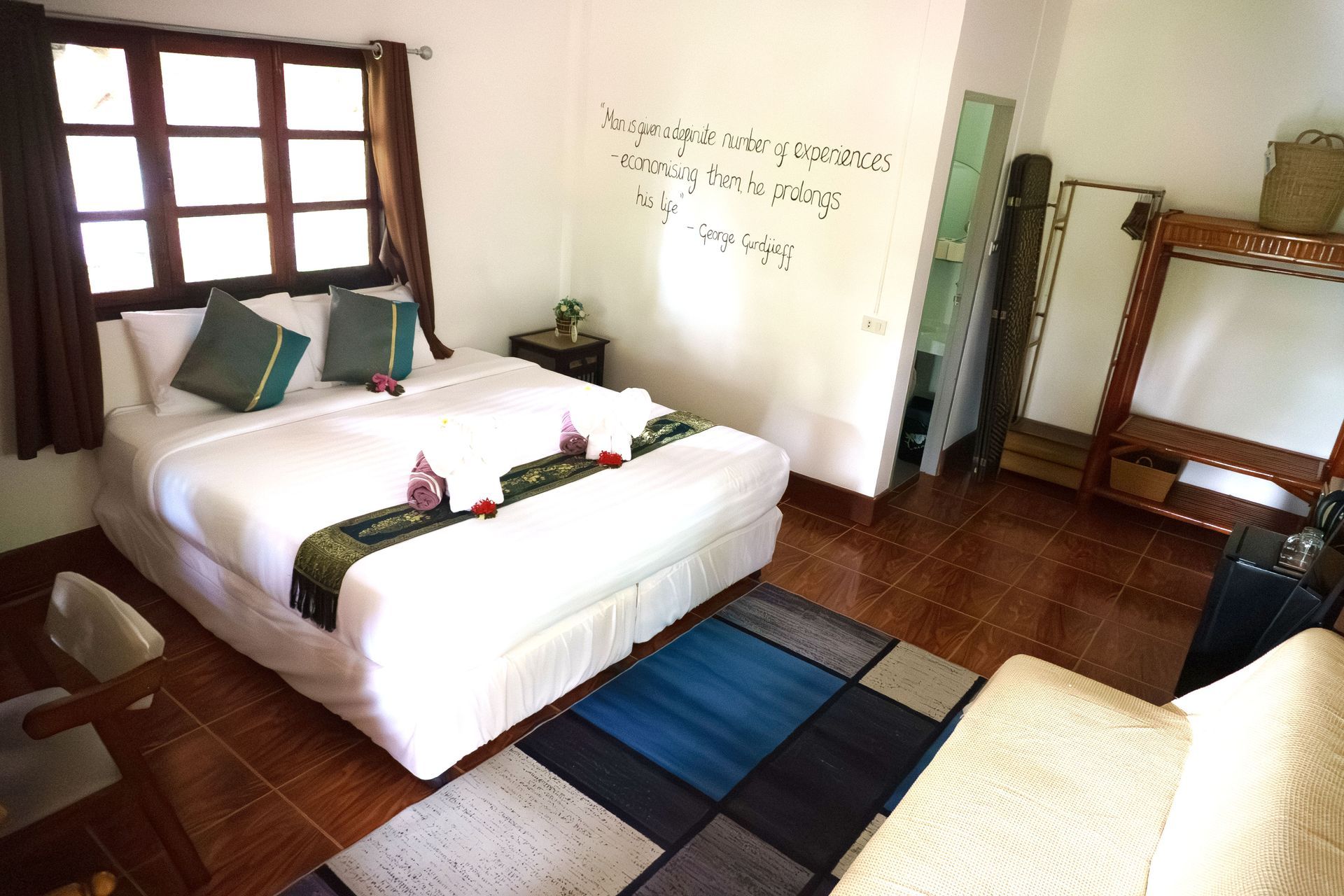 Bright bedroom with white bed, dark wood floor, window, wall mirror, and blue-black rug.