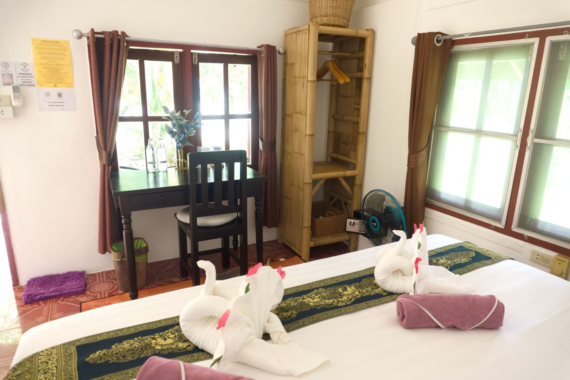 Bright bedroom with a bed, desk by a window, chair, and white towel animals on the bed