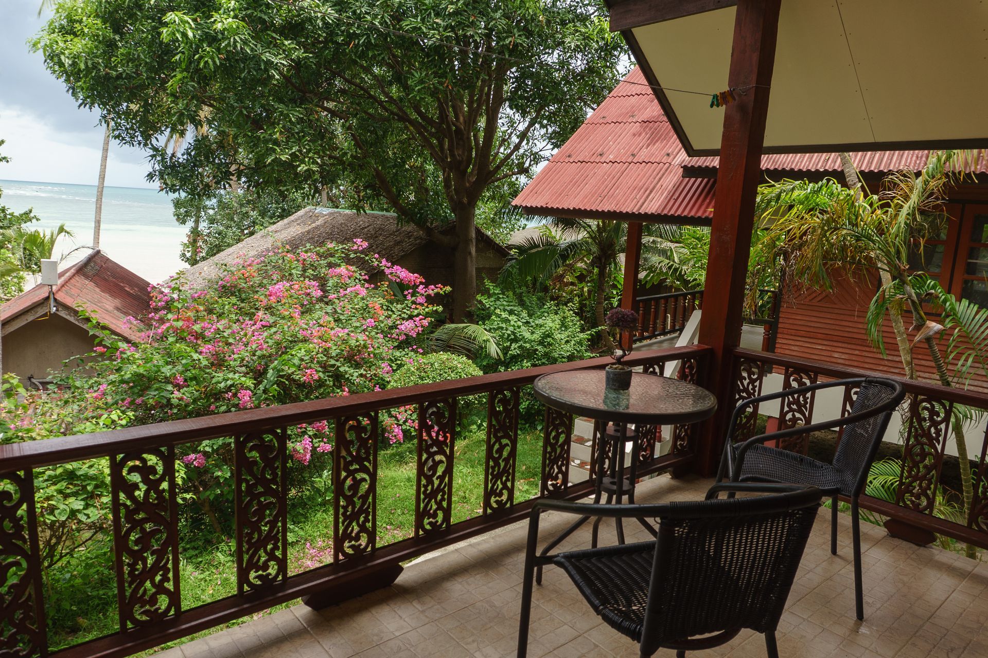 Covered balcony with chairs and table overlooking lush green garden and pink flowers