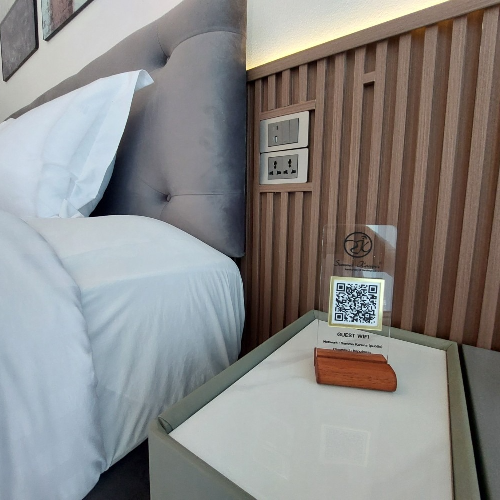 Hotel bedside table with QR code sign beside a bed and padded headboard on a wooden wall panel background