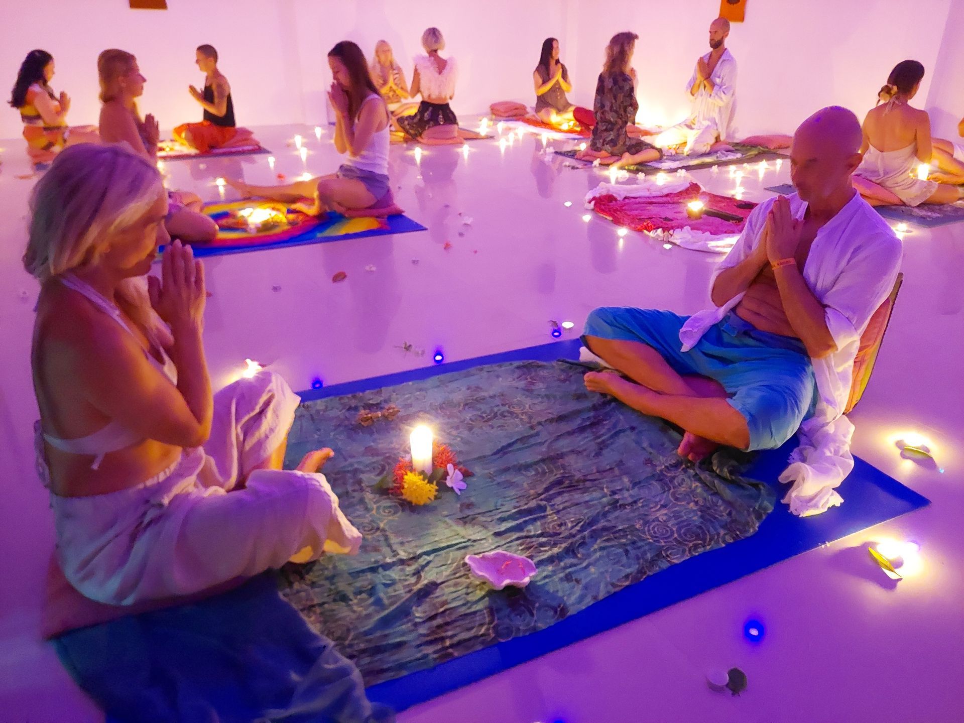 People seated around glowing candles on mats in a softly lit meditation or ceremony room