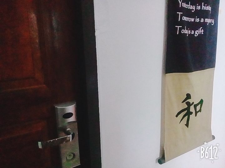 Open wooden door with a silver lock beside a hanging black-and-white wall scroll.