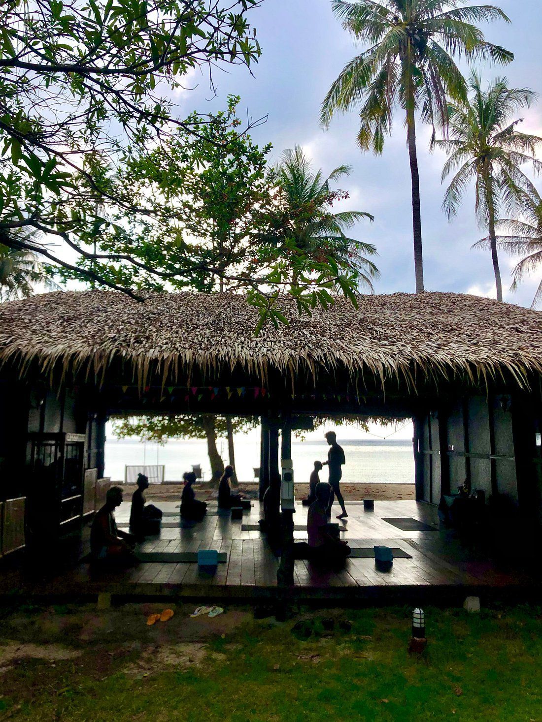 Thatched beach pavilion with silhouetted people and tall palm trees overlooking the ocean