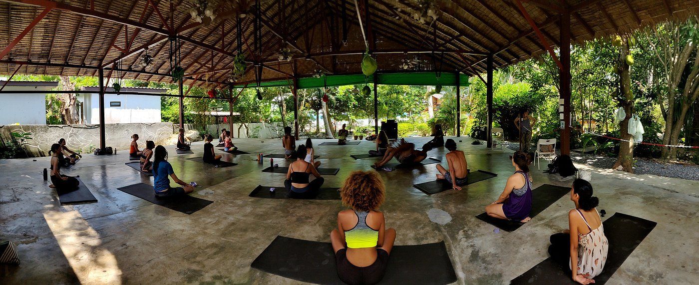 Group seated on mats in an open-air yoga pavilion, facing forward during a meditation session.