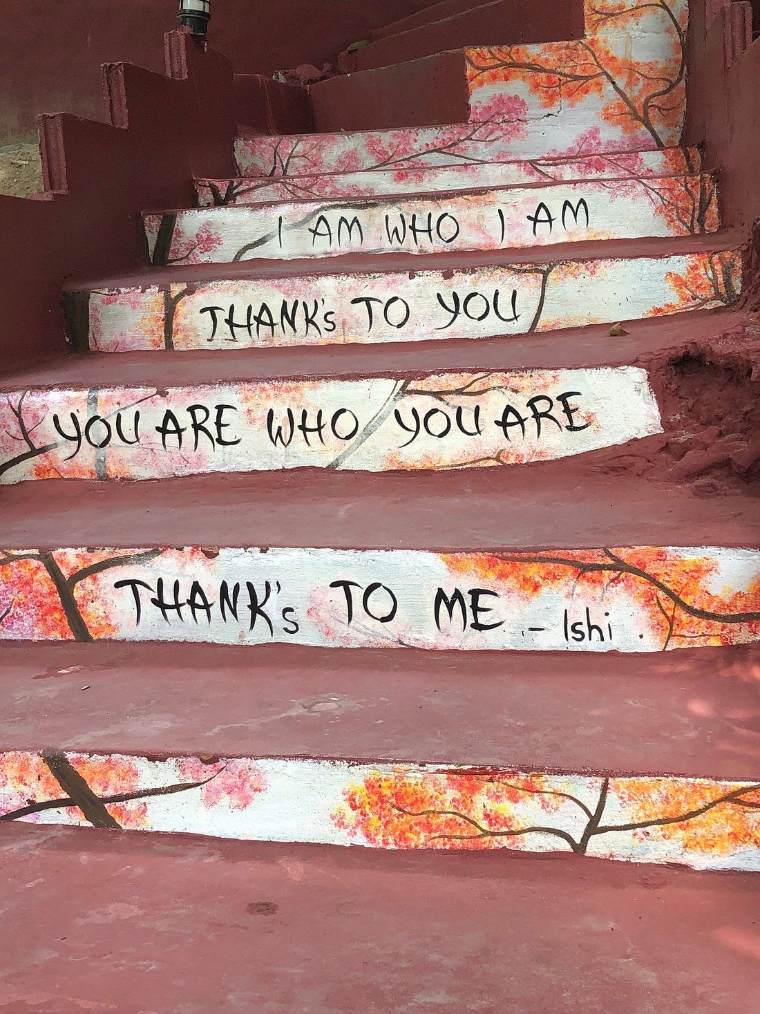 Painted stairs with colorful floral patterns and hand-lettered phrases: “I am who I am,” “Thanks to you,” “You are who you are”