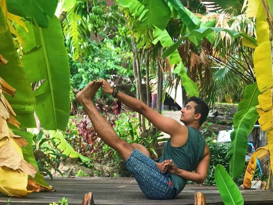 Person doing a yoga pose on a wooden path in a lush tropical garden