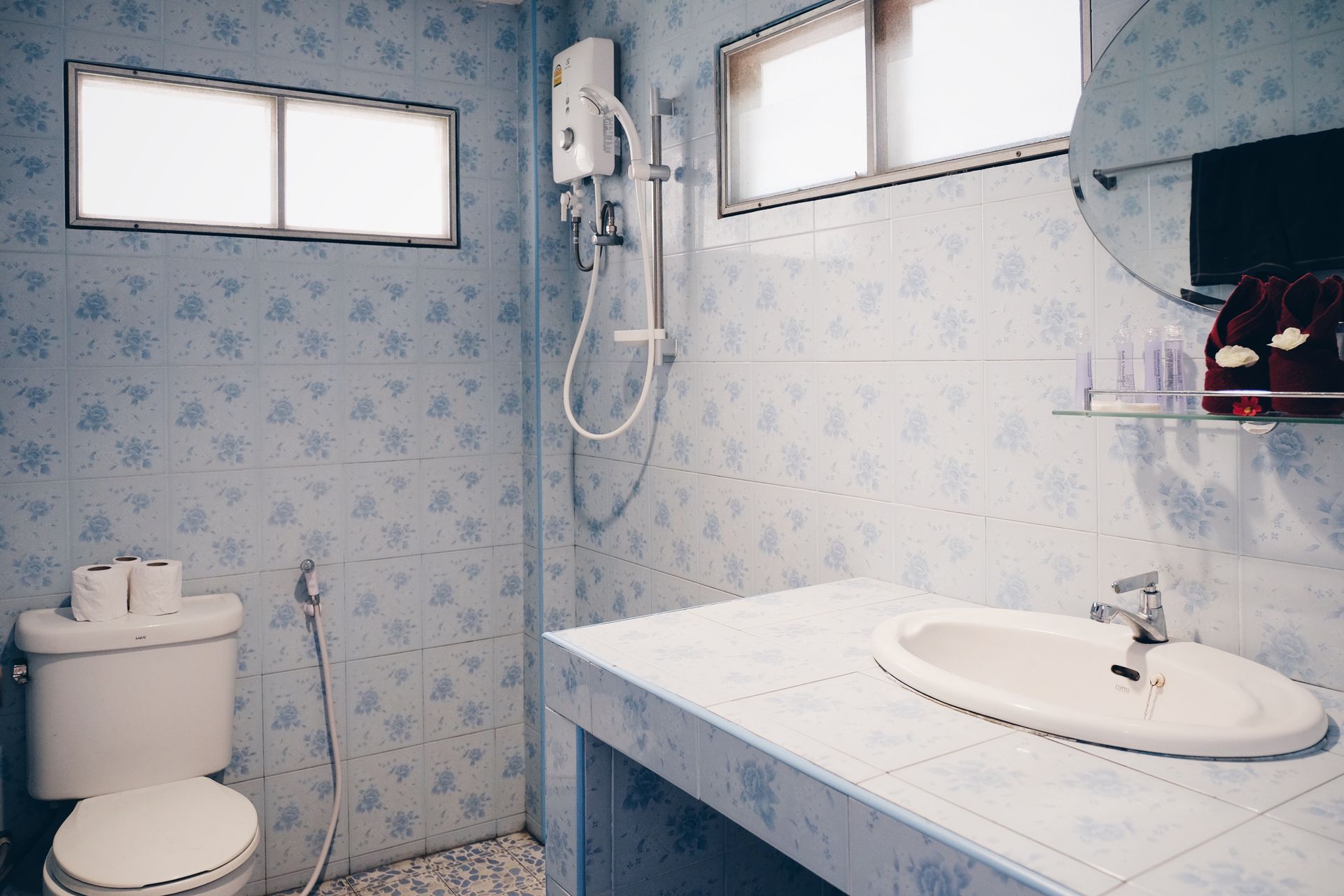 Blue-tiled bathroom with a toilet, sink, shower, and a small window.