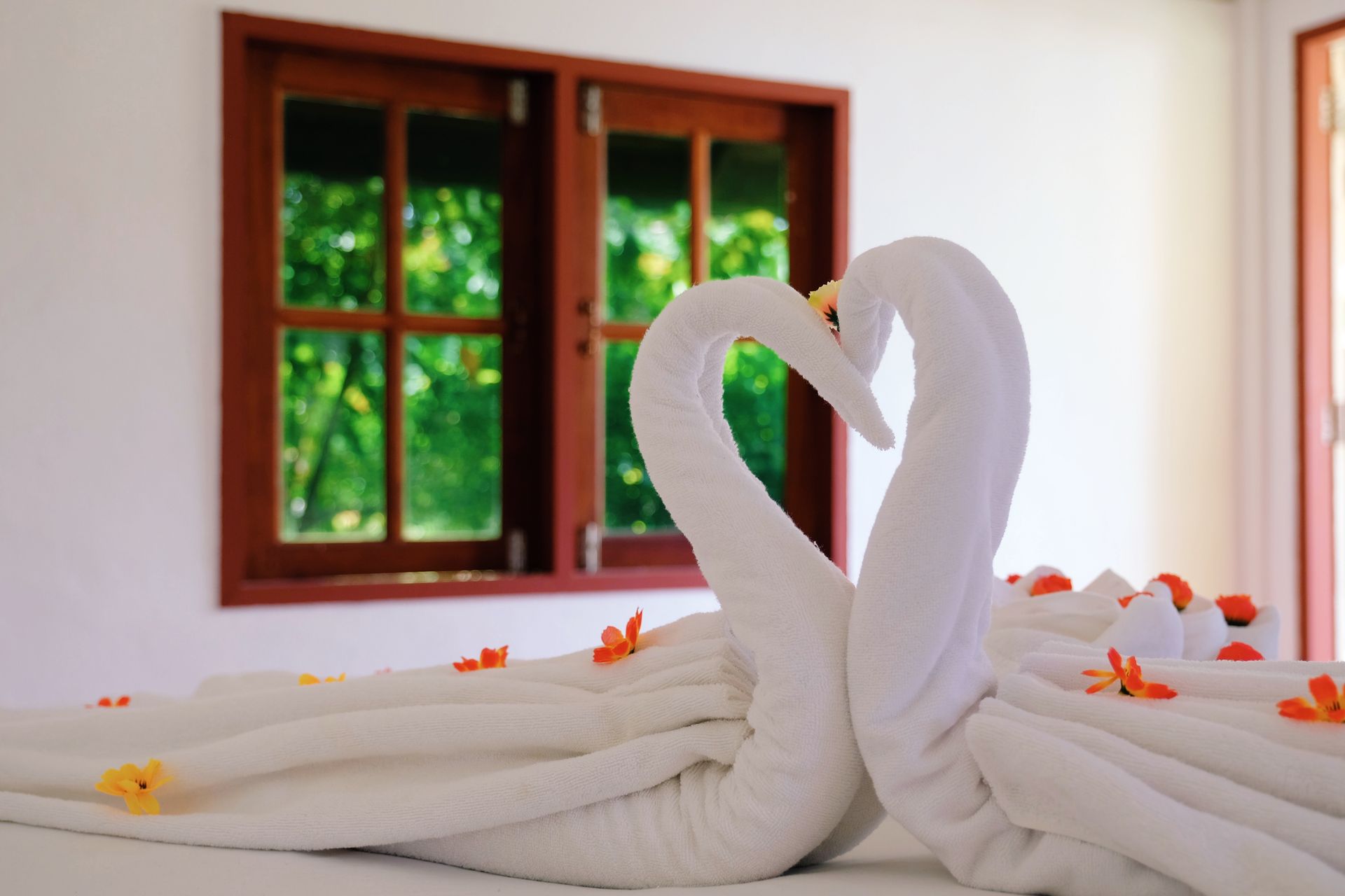 White towel swans with red petals on a bed in a bright room near a wooden window
