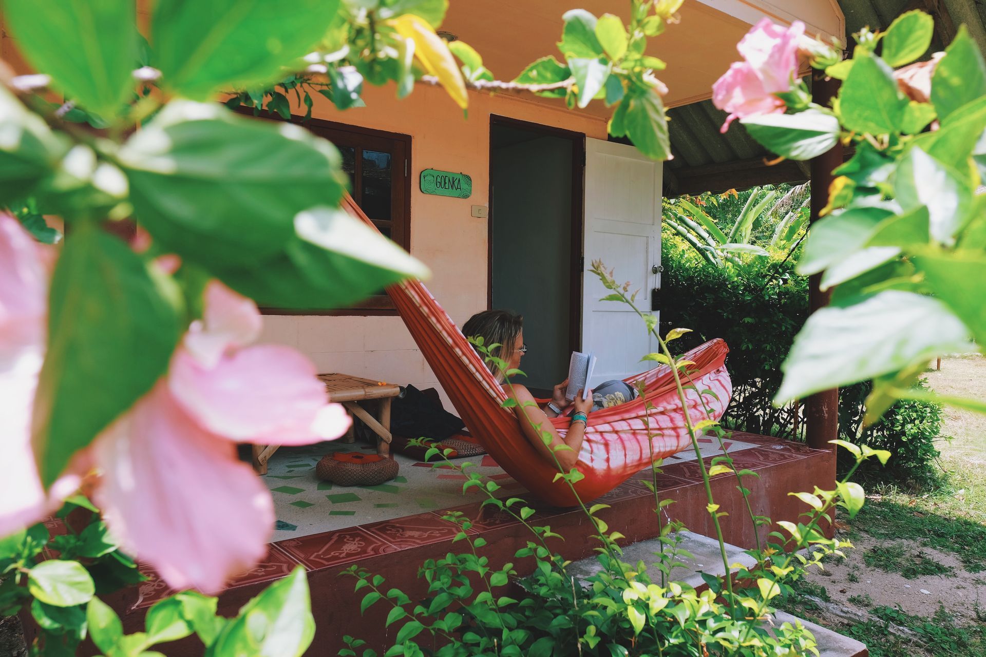 Tropical cottage porch with pink flowers and a red-striped hammock in the shade