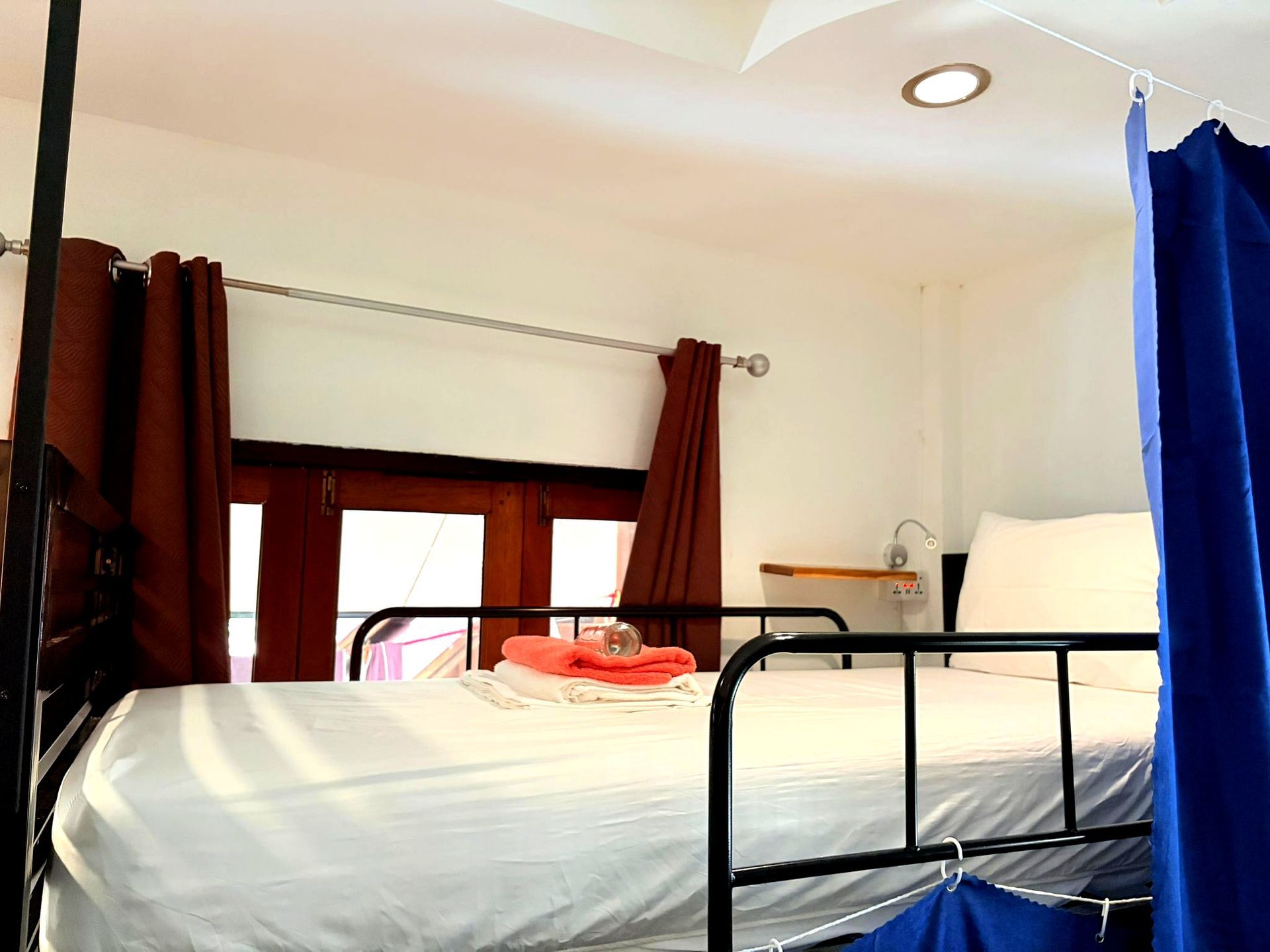 Cozy bedroom with white bedspread, red curtains, window, and blue drape beside a lamp.