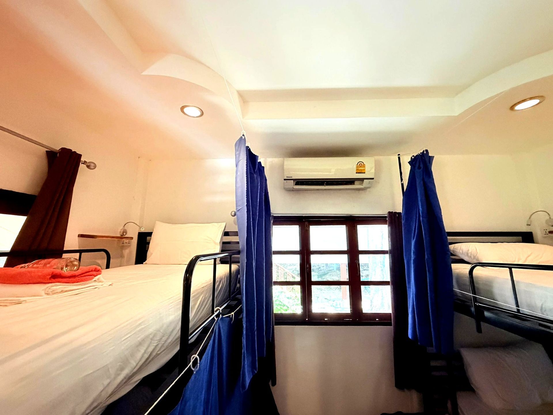 Bright dorm-style room with two bunk beds, blue curtains, and a window air conditioner.