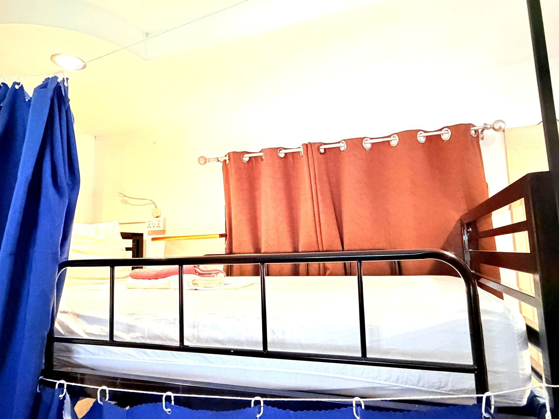 Bedroom with a black metal bed, white bedding, coral curtains, and blue drapes in warm light.
