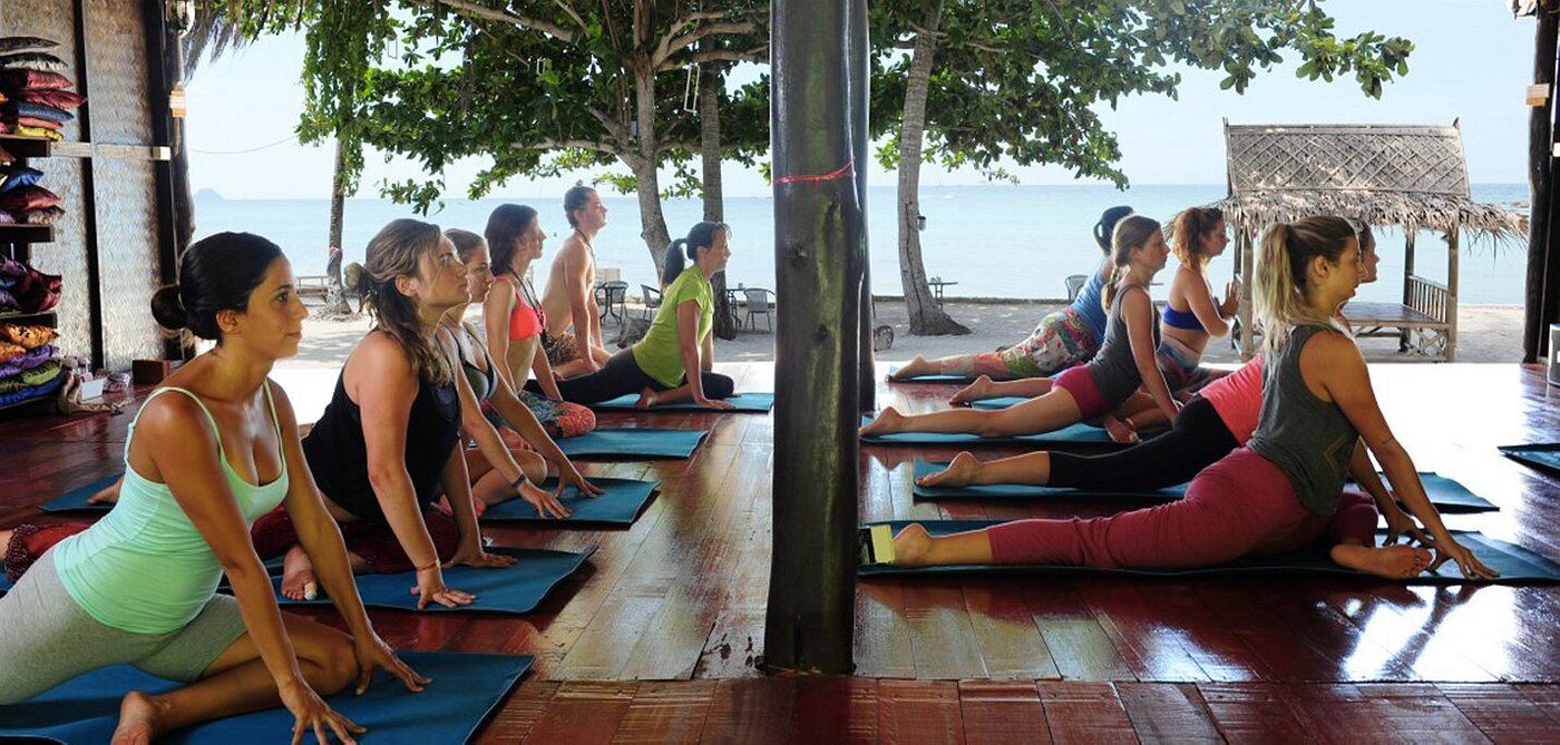 Group practicing yoga on mats in a shaded outdoor pavilion by the water