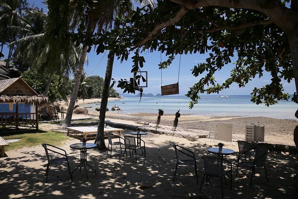 Shaded beach café with tables overlooking a sunny sandy shore and calm ocean waves