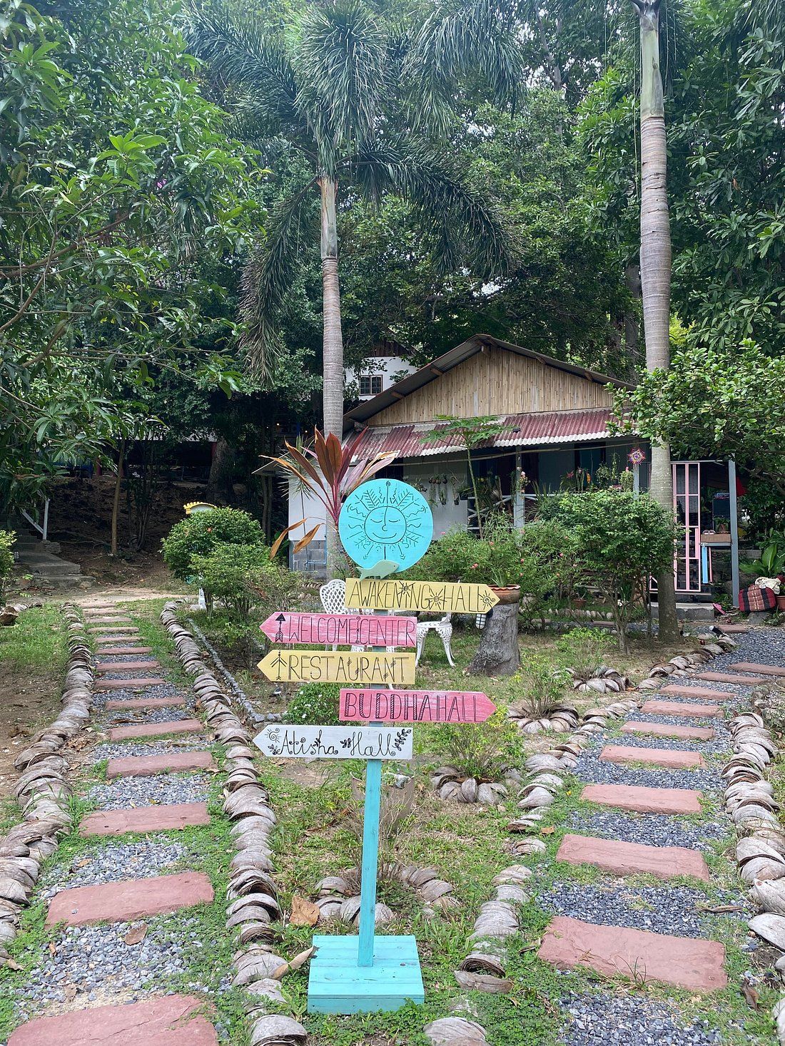 Rustic cabin entrance with stone path, pink signs, and a turquoise signpost amid lush forest greenery