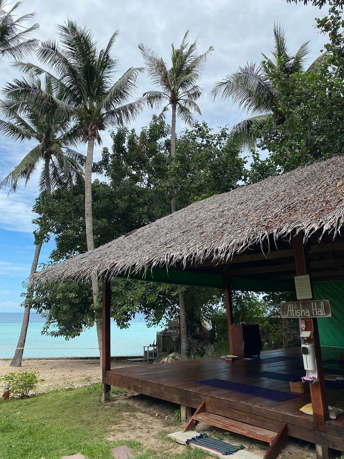 Thatched beach hut with wooden benches under palm trees beside a turquoise sea