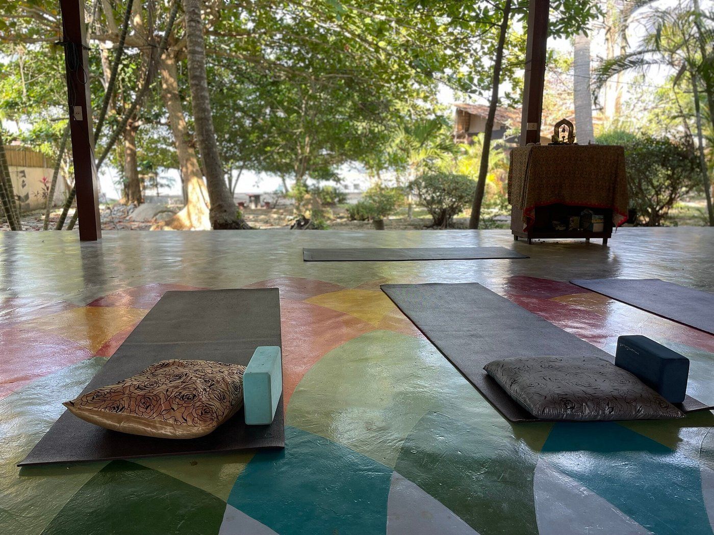 Two yoga mats on a colorful wet floor in an open-air pavilion with trees beyond