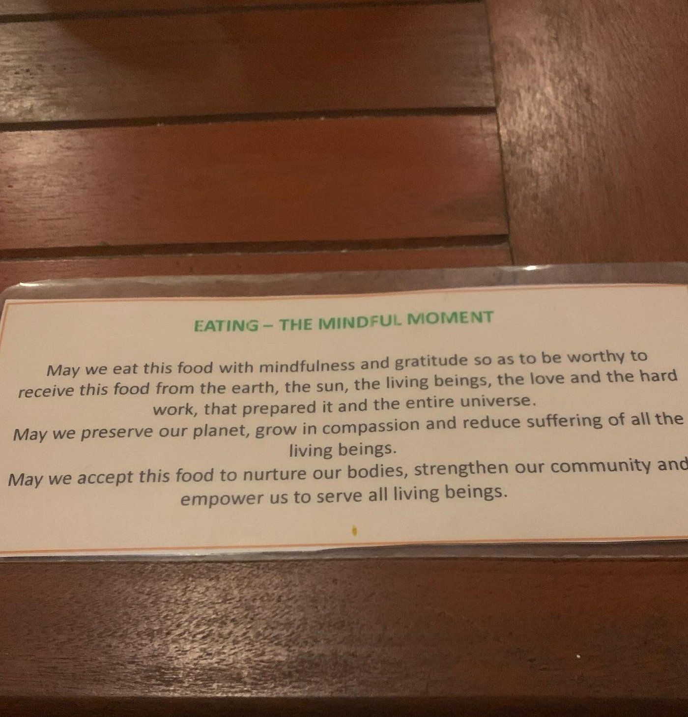 Printed sign on wooden wall about mindful eating and respect for food and living beings.
