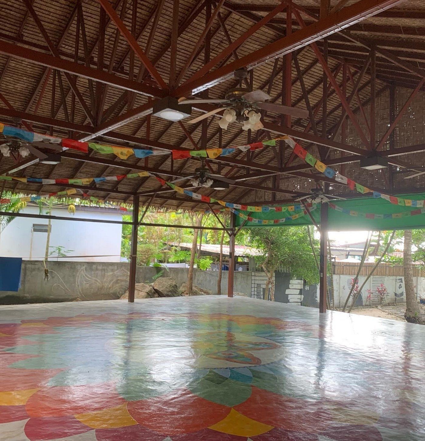 Covered outdoor court with a colorful painted floor and metal roof trusses overhead.