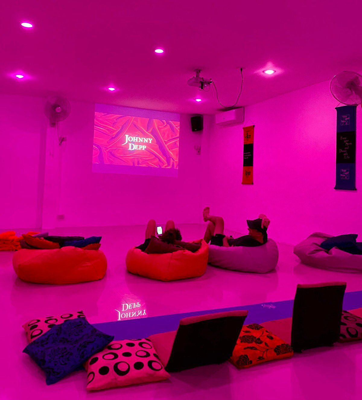 Magenta-lit lounge with people on beanbags watching a projected presentation on the wall