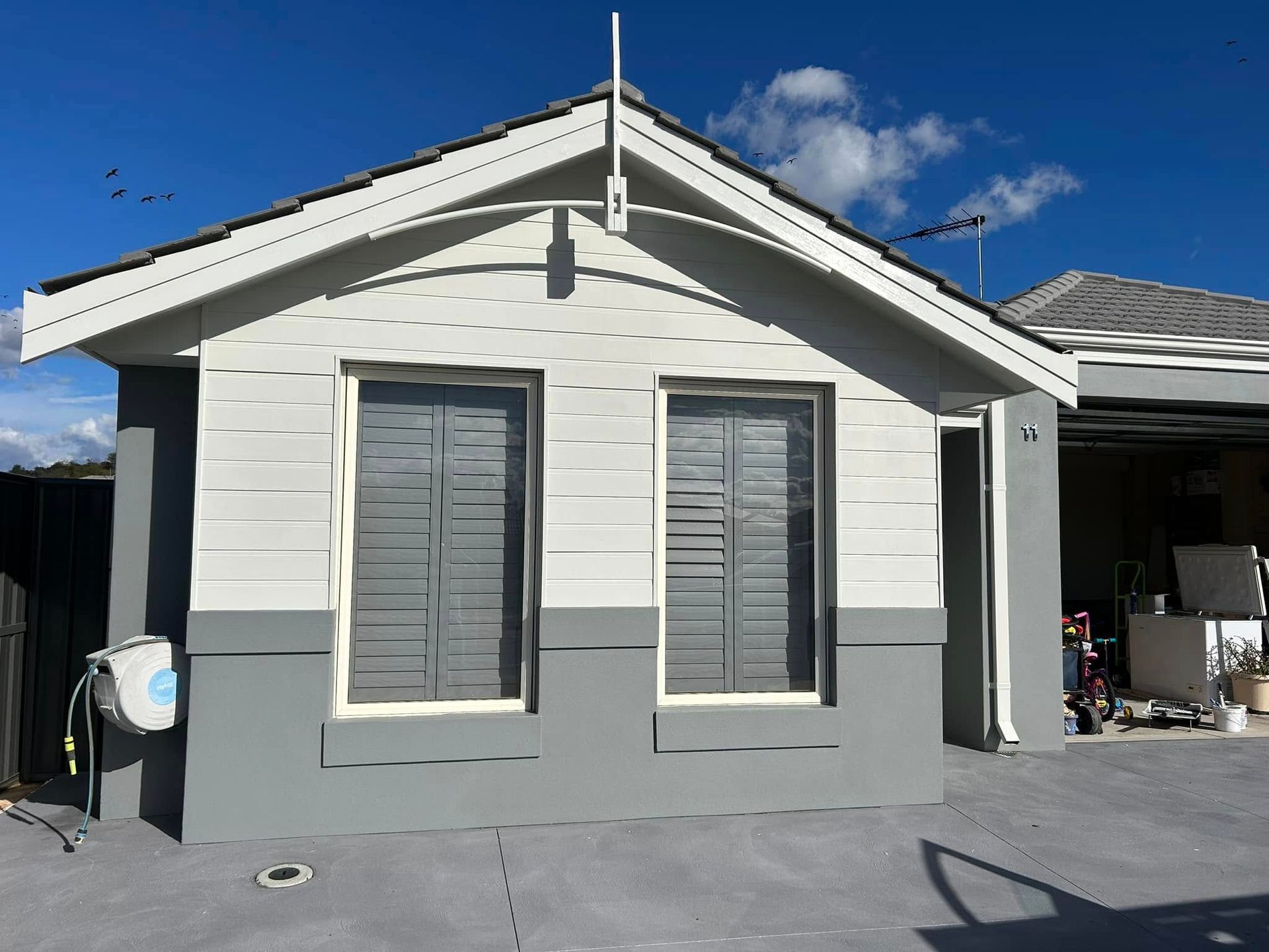 Small white house exterior with gray trim and two front windows under a blue sky